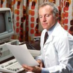 man reading papers in front of computer